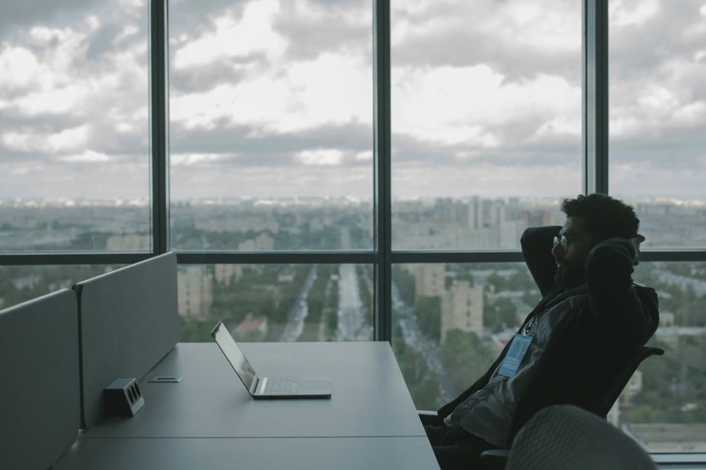 Crafting Captivating Headlines: Your awesome post title goes here A man sits in an office with hands on head in front of a laptop, overlooking a cityscape.